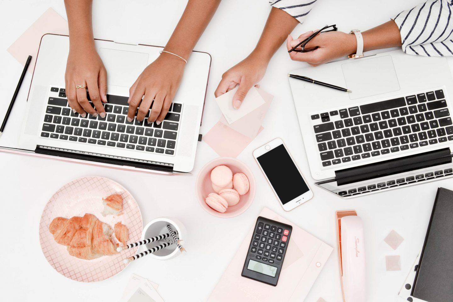 two people working on a white laptop with snacks and phone