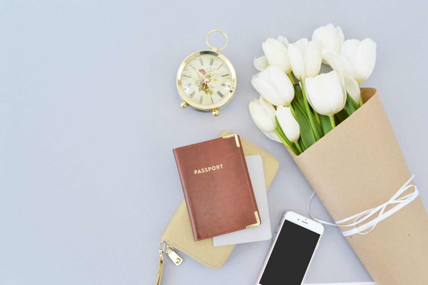 a brown passport wiht flowers, a clock, phone and wallet, travel documents and essentials