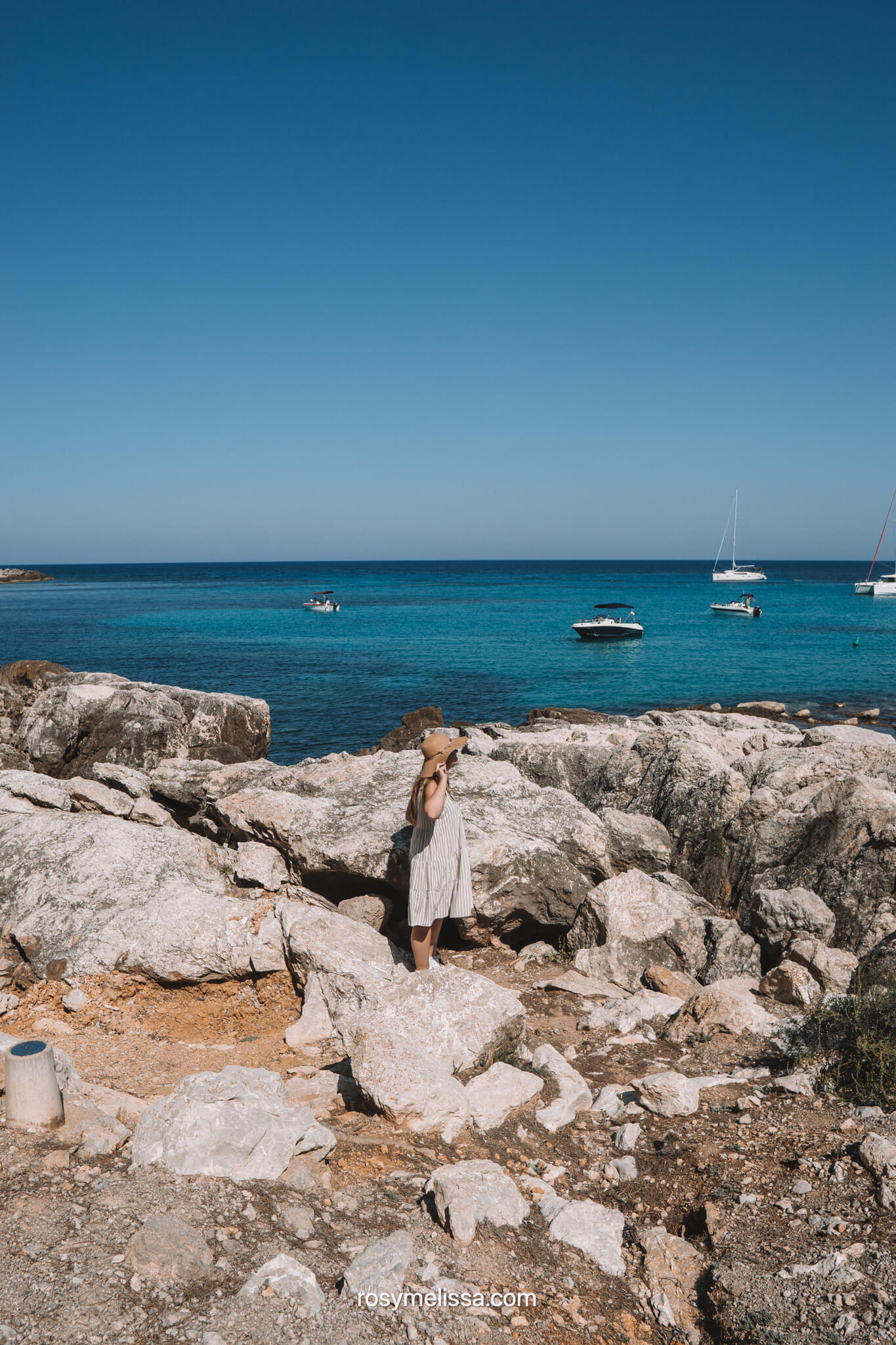 girl in dress and hat looking over the ocean in mallorca